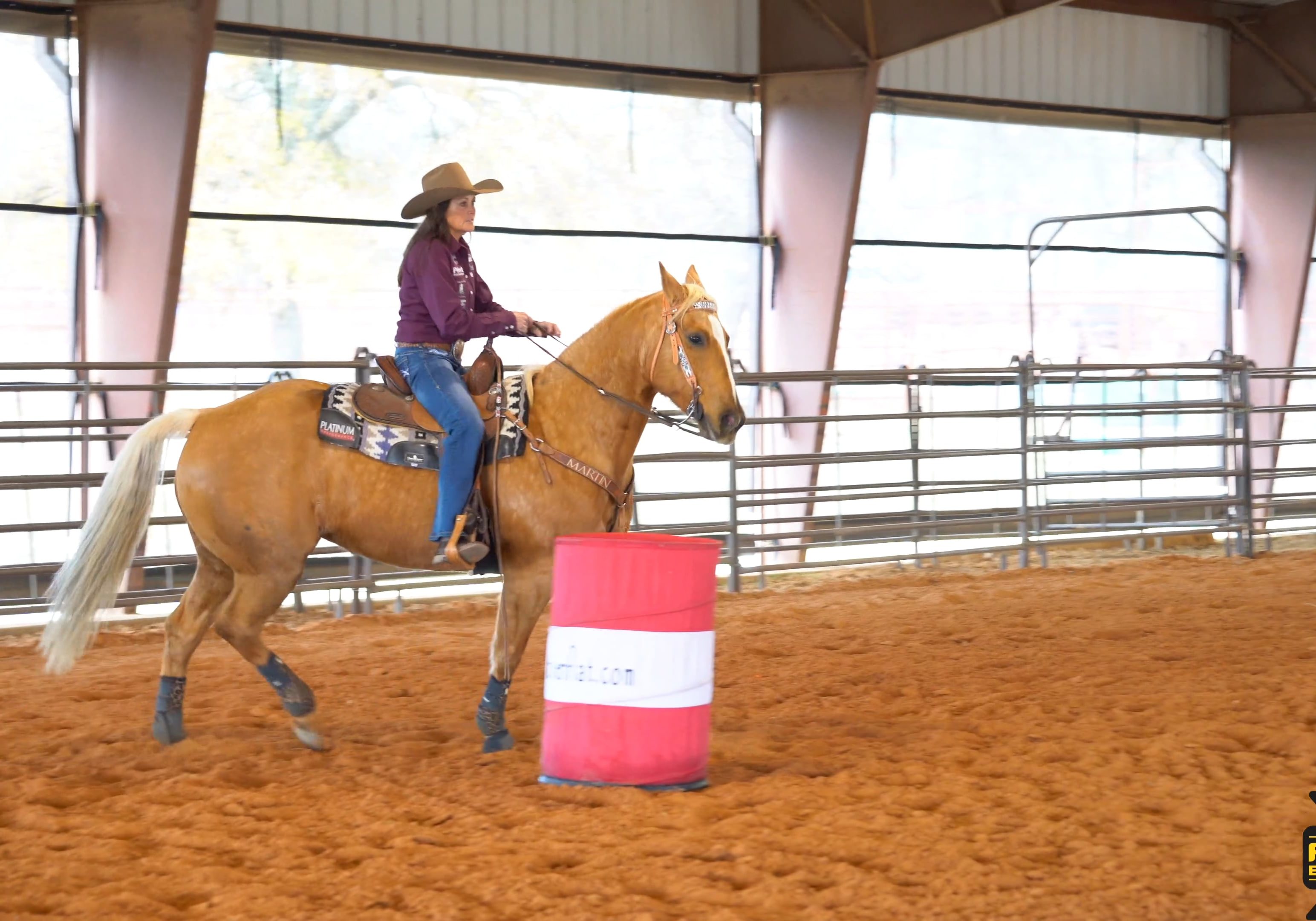 Lisa Lockhart wearing barrel racing attire and riding a horse around a barrel.